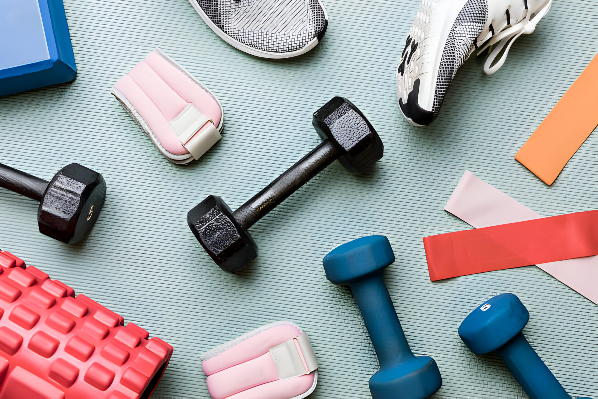 A collection of fitness gear including dumbbells, resistance bands, ankle weights, and shoes, arranged on a yoga mat."